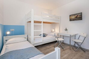 Un dormitorio con literas, un escritorio, dos sillas, una mesita de noche y un televisor montado en la pared.