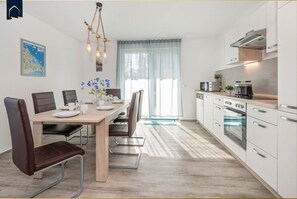 Cozinha moderna com armários brancos, eletrodomésticos de aço inoxidável e um espaço de refeições com mesa e cadeiras de madeira.