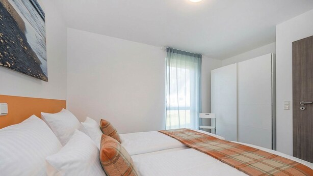 A hotel room with a bed, a window with curtains, a wardrobe, and a painting on the wall.