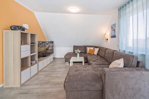 A modern living room with a sectional sofa, a flat-screen TV, a cabinet, and a window with sheer curtains.