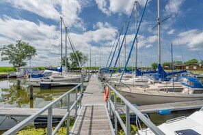 A marina with multiple boats docked, a wooden walkway leading to the boats, and a clear sky.