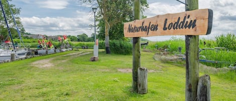 A wooden sign with the text 'Naturhefen Loddi' in a rural setting with boats and a grassy area.