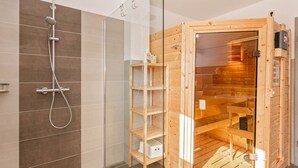 Un baño moderno con ducha, mampara de vidrio y sauna de madera.