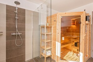 Ein modernes Badezimmer mit Dusche, einer Glastrennwand und einer Holzsauna.