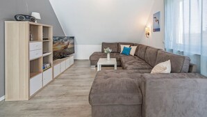Una sala de estar moderna con un sofá seccional, un televisor de pantalla plana, un mueble de madera y una ventana con cortinas.