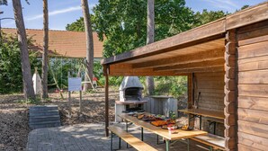 Una estructura de madera al aire libre con un horno de leña incorporado, mesas de picnic y un área pavimentada.