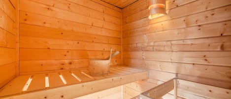 A wooden sauna with benches, a bucket, and a wall-mounted thermometer.