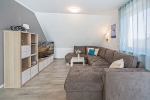 Un salon moderne avec un canapé d’angle, un téléviseur à écran plat, un meuble en bois et une fenêtre avec des rideaux.