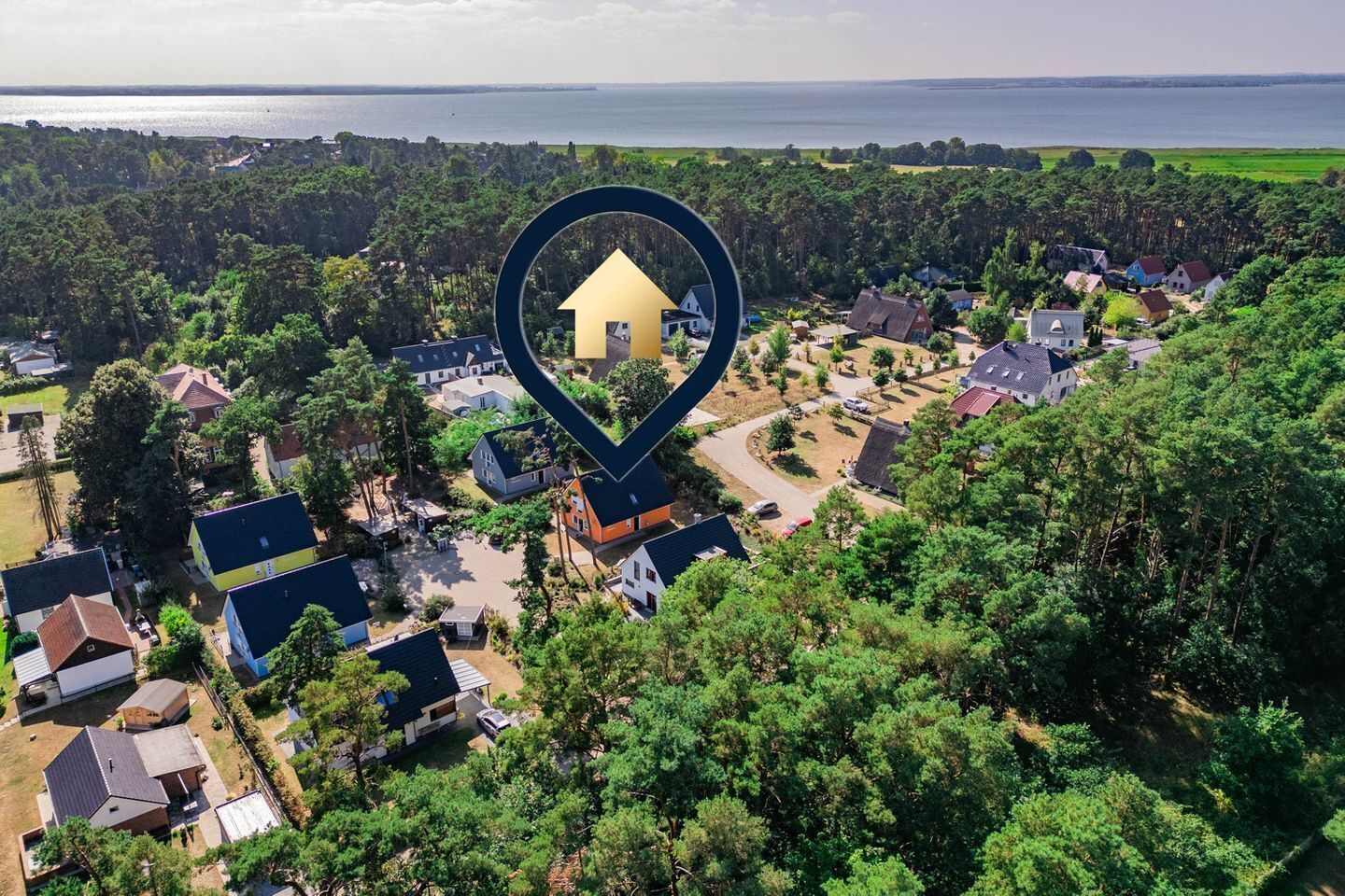 Luchtbeeld van een woonwijk met huizen, omgeven door weelderige begroeiing en een waterpartij op de achtergrond.