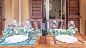 Una mesa de comedor lista con platos, cubiertos y copas de vino, con una botella de vino y plantas decorativas sobre la mesa.