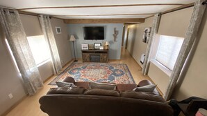 Een woonkamer met een bruine bank, een kamerkleed met patroon, een televisie en een houten kast.