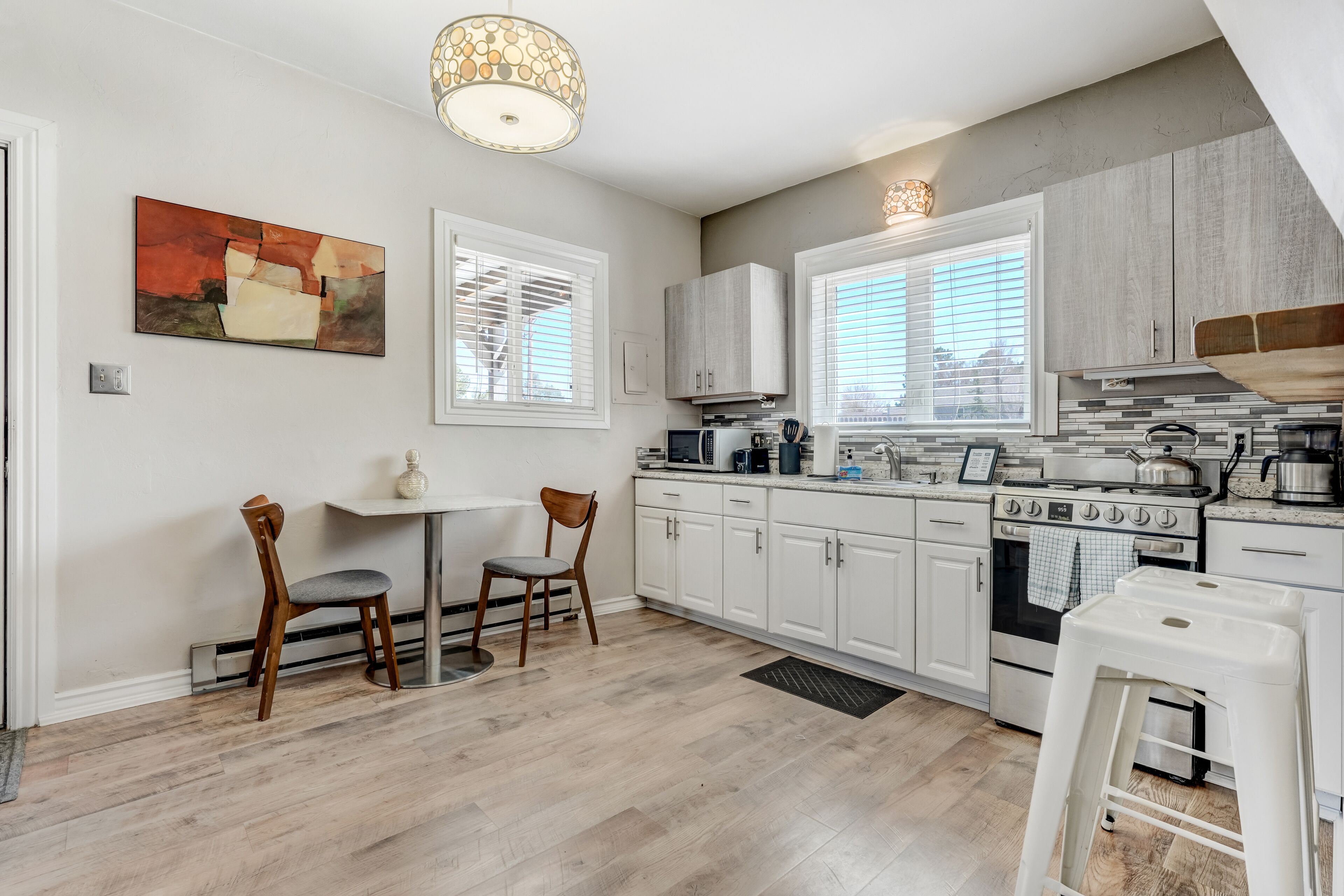A modern kitchen with white cabinets, a dining table with chairs, and a hanging light fixture.