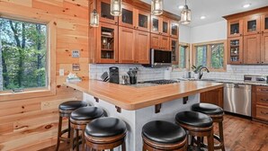 Cozinha moderna com armários de madeira, uma ilha grande com banquetas, eletrodomésticos de aço inoxidável e vista para a floresta.