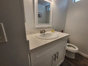 Un bagno con un lavandino bianco, uno specchio, un water e un armadietto.