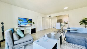 Una sala de estar moderna con una televisión de pantalla plana, un sofá, una mesa de centro y un comedor con una silla y una mesa.