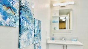 Un baño con un lavamanos y muebles blancos, y dos cuadros azules abstractos en la pared.