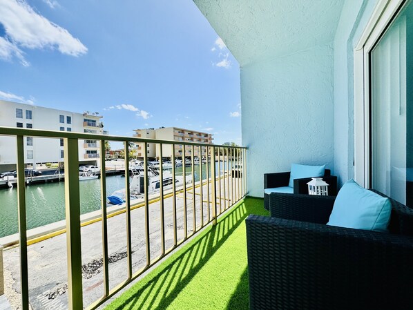 A balcony with a view of a marina, a wicker sofa with cushions, and a small white lantern. - Coastal Charm: Waterfront, Free Parking, walk to the beach (North Miami Beach)