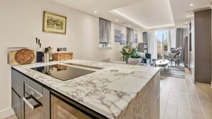 A modern kitchen with a marble countertop, a built-in oven, and a dining area with a table and chairs. - Canal Side Luxury 1 Bed Chelsea (Greater London)