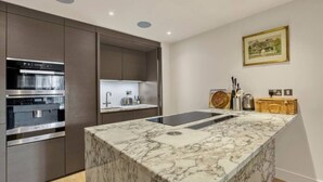 A modern kitchen with built-in appliances, a marble countertop, and a small island. - Canal Side Luxury 1 Bed Chelsea (Greater London)