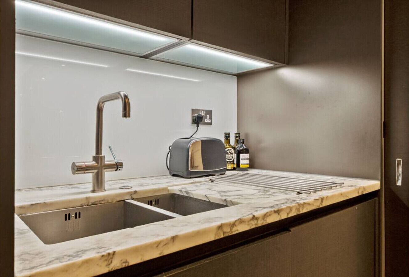 A kitchen with a double sink, a toaster, and a bottle of alcohol on the counter.