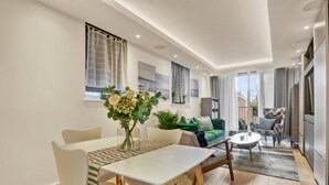 A modern living room with a dining area, a sofa, a coffee table, and a decorative plant. - Canal Side Luxury 1 Bed Chelsea (Greater London)