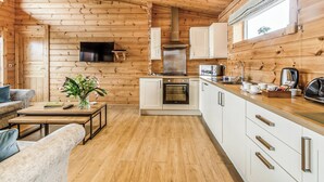 A wooden cabin interior with a kitchen, dining area, and a TV mounted on the wall.