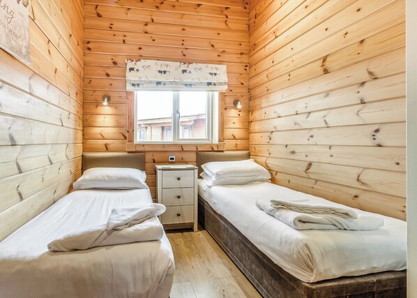 A cabin-style room with two beds, a window with a curtain, a nightstand, and a thermostat.