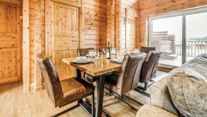 A wooden cabin interior with a dining table set for six, leather chairs, and a large window offering a view.