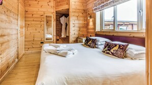 A wooden cabin room with a bed, a mirror, a robe, and a window.
