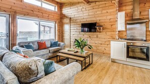 A log cabin interior with a sofa, coffee table, TV, and kitchen area.