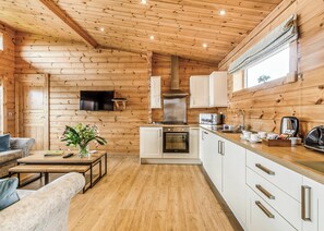 A wooden cabin interior with a kitchen, dining area, and a TV mounted on the wall.