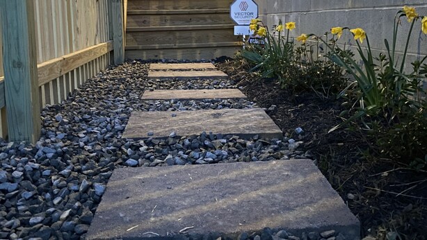 A pathway leading to a house with a wooden fence and a sign indicating security.