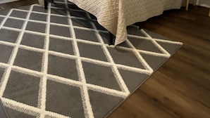 A bedroom with a bed, a rug, a nightstand, a lamp, and wall shelves.