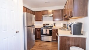 A compact kitchen with wooden cabinets, a stainless steel refrigerator, an oven, and a coffee maker.