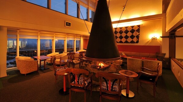 Relax in a warm and inviting lounge area with a central fire feature, comfortable seating, and city views.
