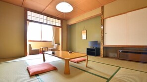 Traditional Japanese-style room with tatami flooring, featuring a low table, TV, and cabinet.