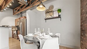 A modern dining area with a round table set for four, white chairs, and a hanging light fixture above. - Intimate 2BD with Unique Style in the heart of FW (Fort Worth)