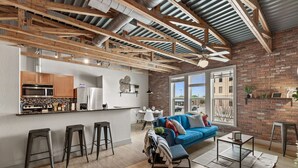 A modern kitchen with stainless steel appliances, a dining area with a blue sofa, and a large window offering a view of the outside. - Intimate 2BD with Unique Style in the heart of FW (Fort Worth)