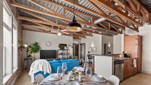 A dining area with a table set for four, a blue sofa, and a kitchen in the background. - Intimate 2BD with Unique Style in the heart of FW (Fort Worth)