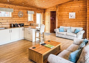 Een houten blokhut van binnen met een keuken, een eethoek en een woonkamer.