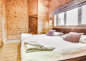Een houten kamer met een bed, kussens, een raam met gordijnen en een houten deur.