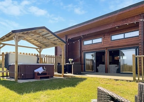 A modern outdoor patio with a hot tub, wooden deck, and a covered seating area.