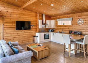 A log cabin interior with a kitchen, dining area, and a living room with a sofa and coffee table.