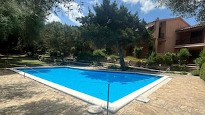 Ein rechteckiger Swimmingpool mit einer Steinterrasse, umgeben von Bäumen und einem Gebäude mit Balkonen.