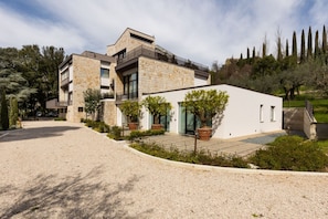 A modern two-story house with a stone facade, a balcony, and a gravel driveway.