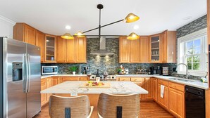 Una cucina moderna con mobili in legno, un frigorifero in acciaio inossidabile, un'isola in marmo e due sedie di legno.