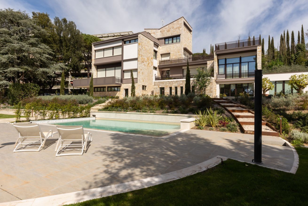 Un edificio moderno a più piani con piscina, area relax all'aperto e giardino curato.