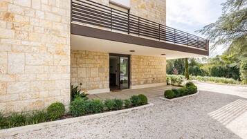 Un edificio moderno con facciata in pietra, un balcone con ringhiera in metallo e una strada di accesso sterrata.