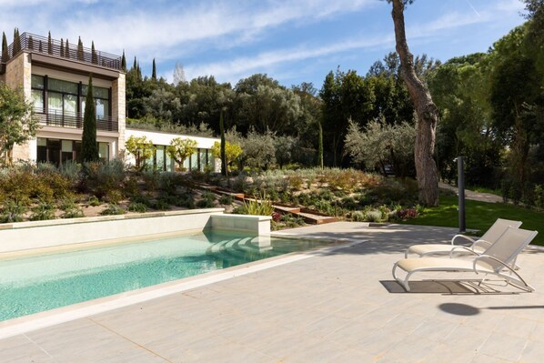 Una casa moderna con piscina, mobiliario exterior y jardín ajardinado.