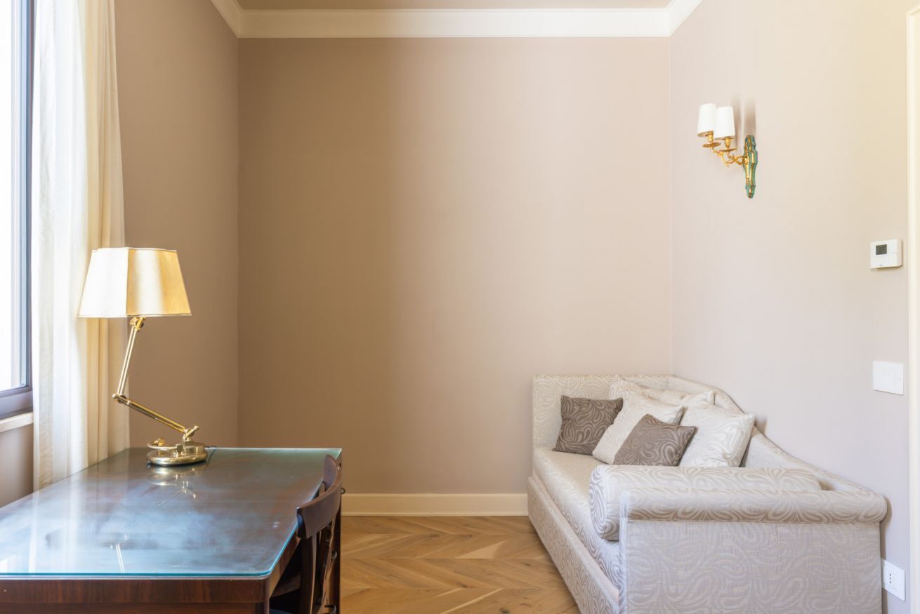 Ein Zimmer mit einem Holztisch, einer Lampe, einer Couch mit gemusterten Kissen und einer Wandleuchte.